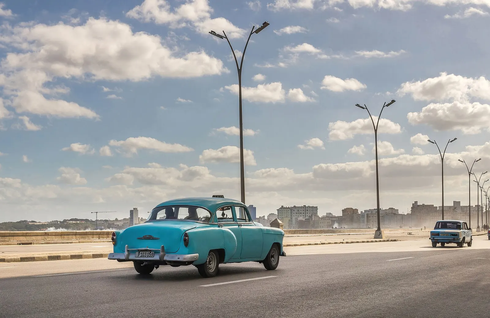 A turquoise vintage car driving along the Malecón in Havana