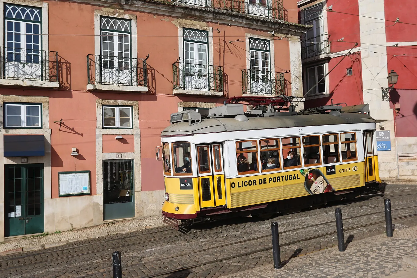Un tramway jaune d'époque devant des façades roses dans l'Alfama, à Lisbonne